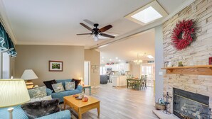 A spacious living room with a fireplace, a ceiling fan, and a dining area with a kitchen in the background. - Home w/ Game Room, Fenced Yard, 8-person Jacuzzi (Banner Elk)