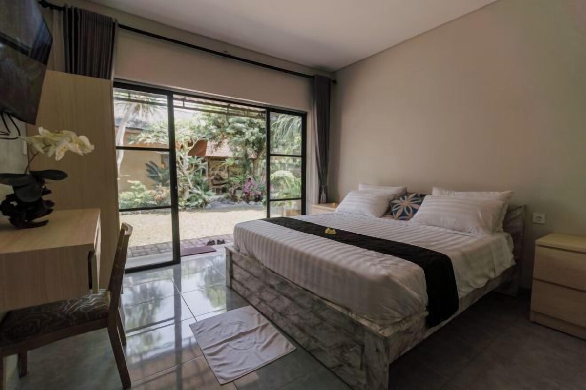 A bedroom with a large bed, a desk, and a view of a garden through a sliding glass door.