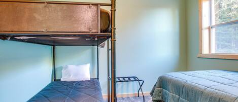 A bunk bed room with a window, a small table, and a bed with a quilted bedspread.