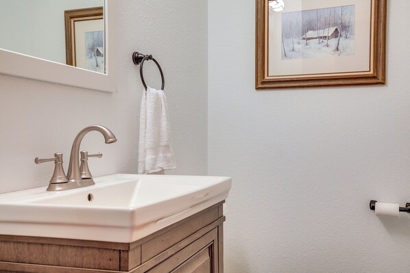 Une salle de bain avec un lavabo blanc, un miroir, un tableau encadré accroché au mur et une serviette suspendue à un porte-serviette.