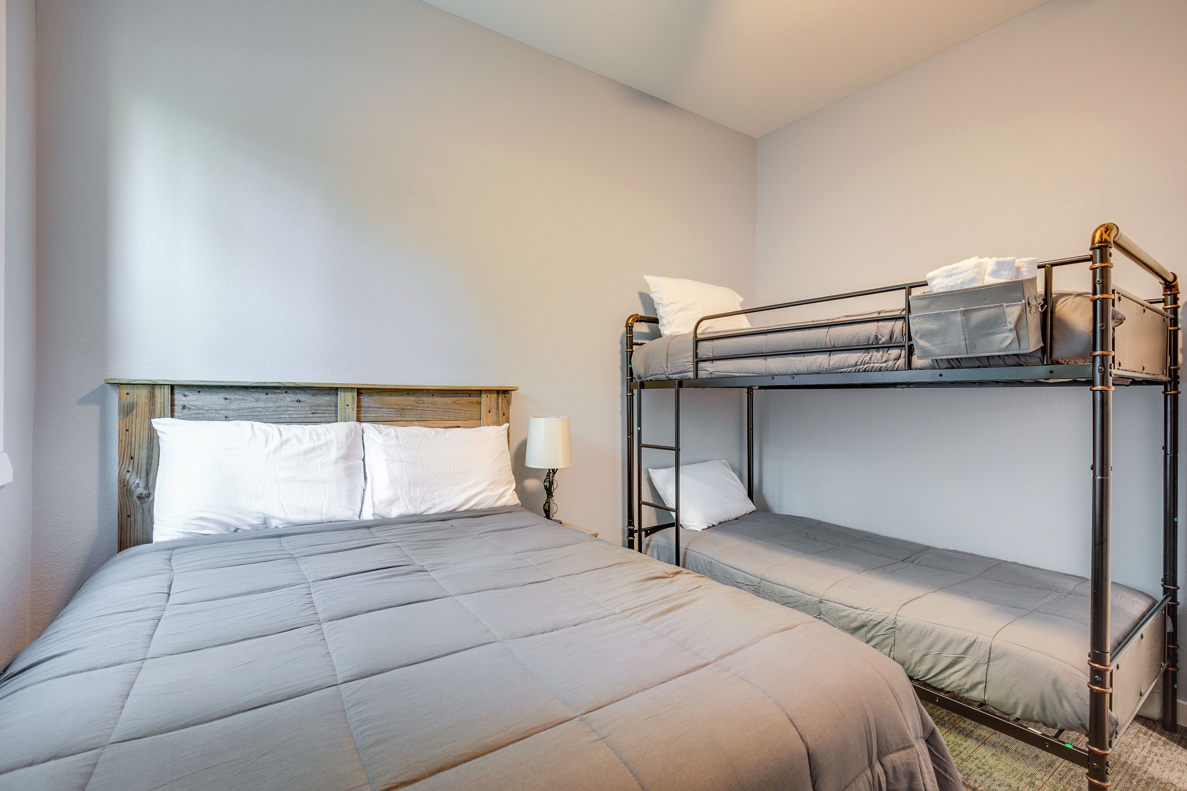 A bunk bed room with a wooden headboard, a single bed, and a nightstand with a lamp.