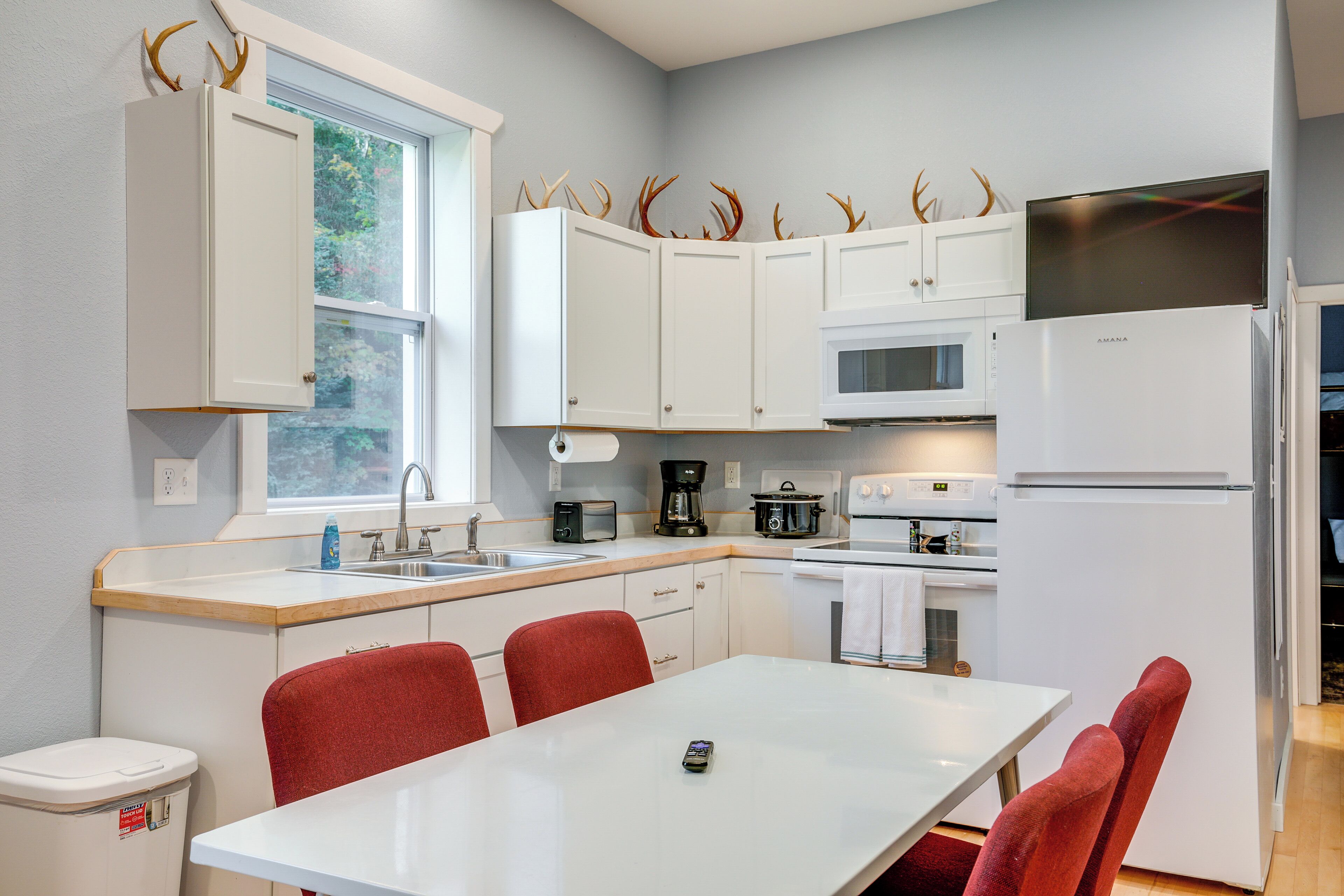 A modern kitchen with white cabinets, a microwave, a stove, and a refrigerator. There is a window with a view of greenery outside.