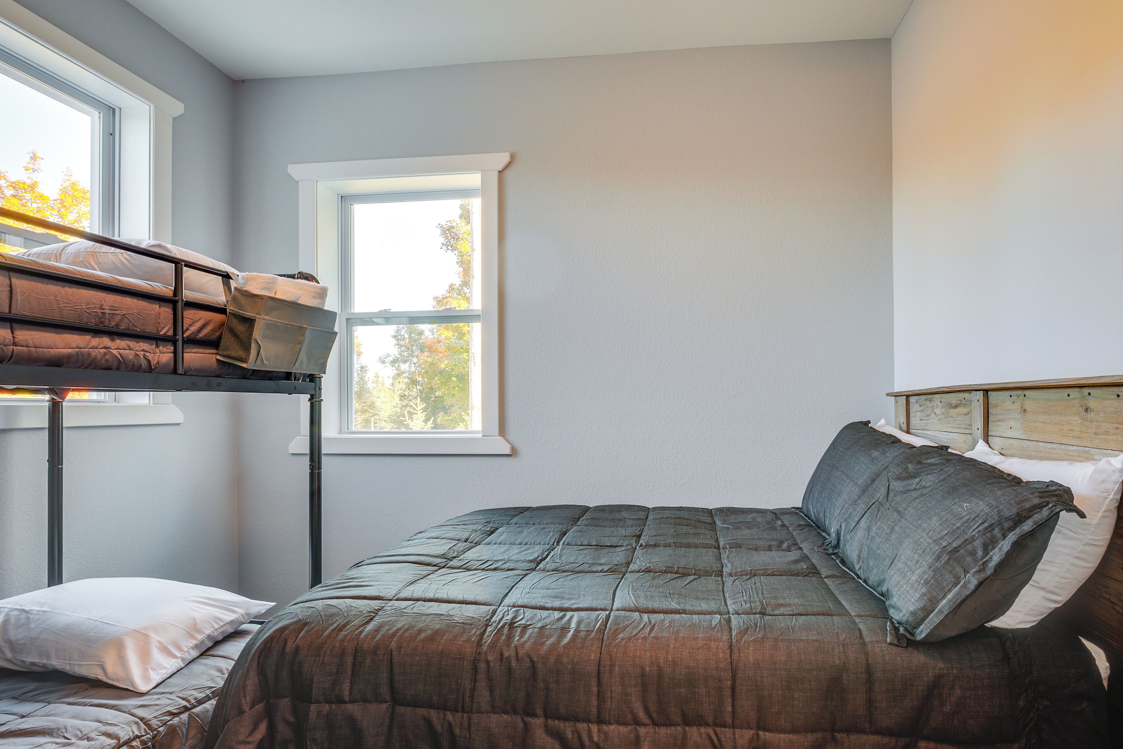 A bedroom with a bunk bed, a single bed, and a window with a view of trees.
