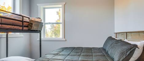 A bedroom with a bunk bed, a single bed, and a window with a view of trees.