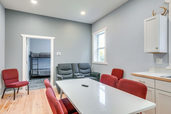 Une pièce comprenant un lit superposé, un canapé gris, une table à manger avec des chaises et un coin cuisine avec un évier.