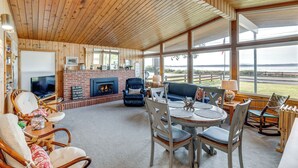 Un salón amplio con chimenea, asientos cómodos y ventanas grandes que ofrecen vistas al exterior.