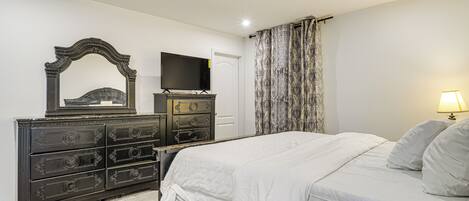 Un dormitorio con cama, cómoda, televisor y cortinas.