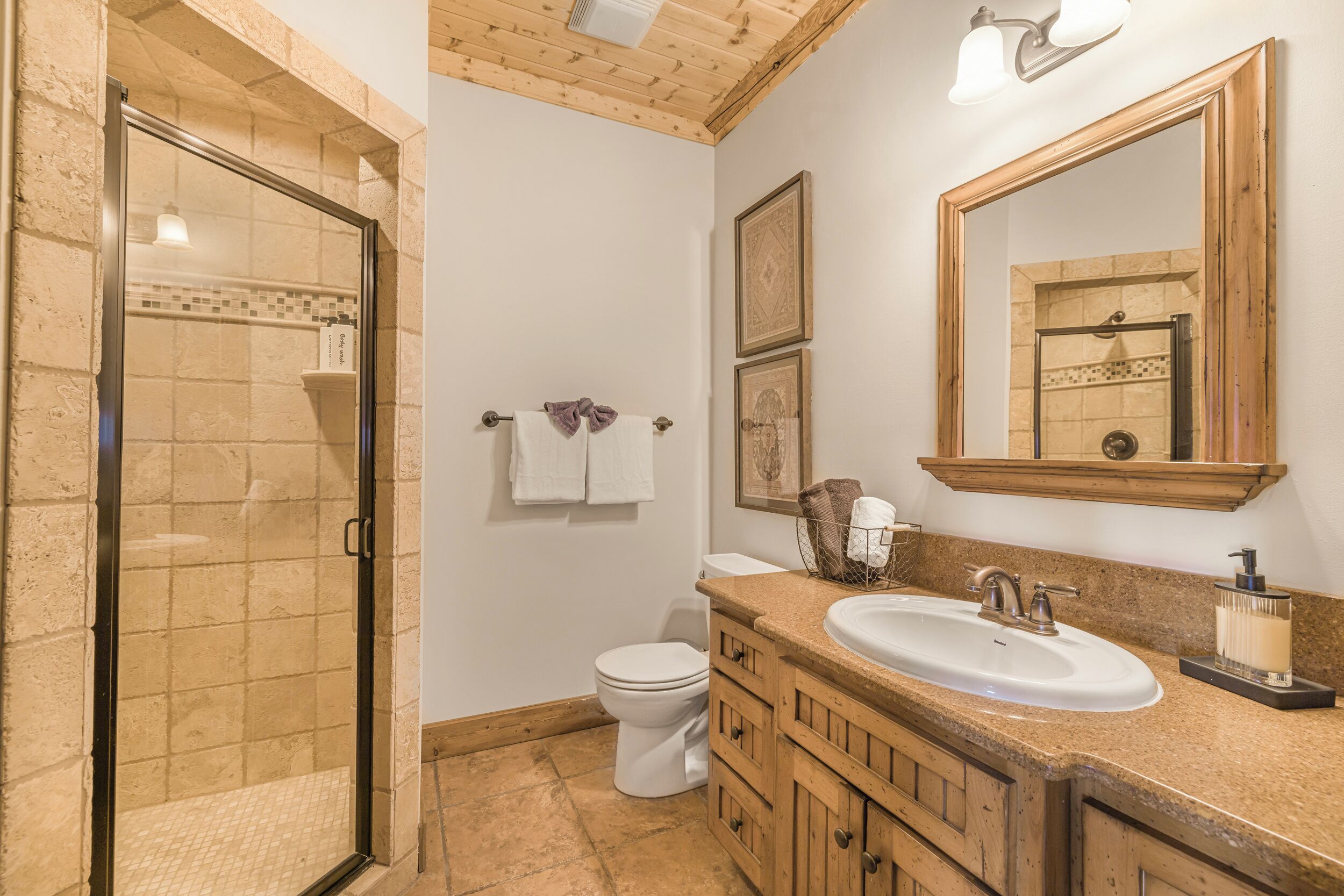 A bathroom with a glass shower enclosure, a white toilet, wooden cabinets, a sink with a mirror, and a towel rack.