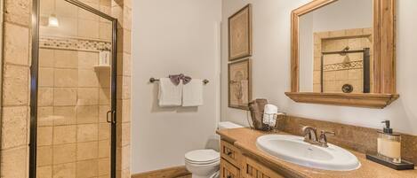A bathroom with a glass shower enclosure, a white toilet, wooden cabinets, a sink with a mirror, and a towel rack.