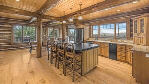 Una cocina amplia con pisos de madera, una isla grande con taburetes de bar, armarios de madera y ventanas grandes que ofrecen vistas al exterior.