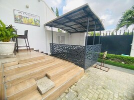 Un área de estar al aire libre techada con una pérgola, una planta en maceta y un letrero de Presken Food & Grill.