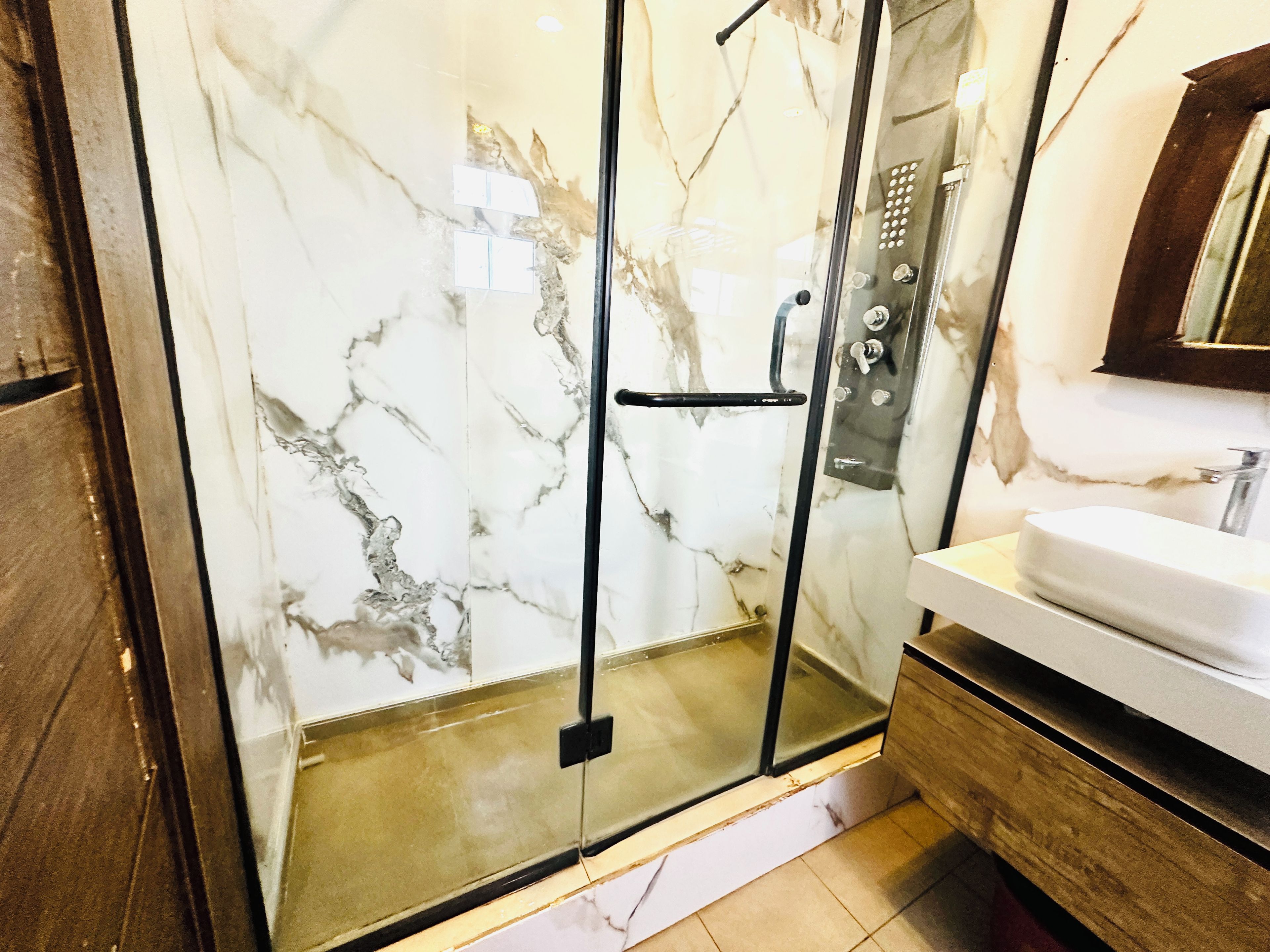 Une salle de bain moderne avec une douche à parois de verre, des murs en marbre et un meuble-lavabo en bois.