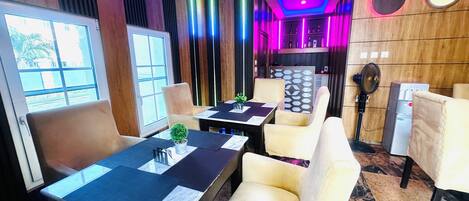 A modern interior with a dining area featuring tables and chairs, a water dispenser, and a fan.