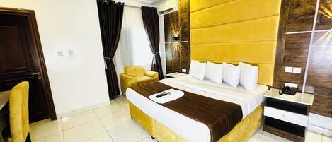 A hotel room with a large bed, a chair, a bedside table with a phone, and a wall-mounted air conditioning unit.