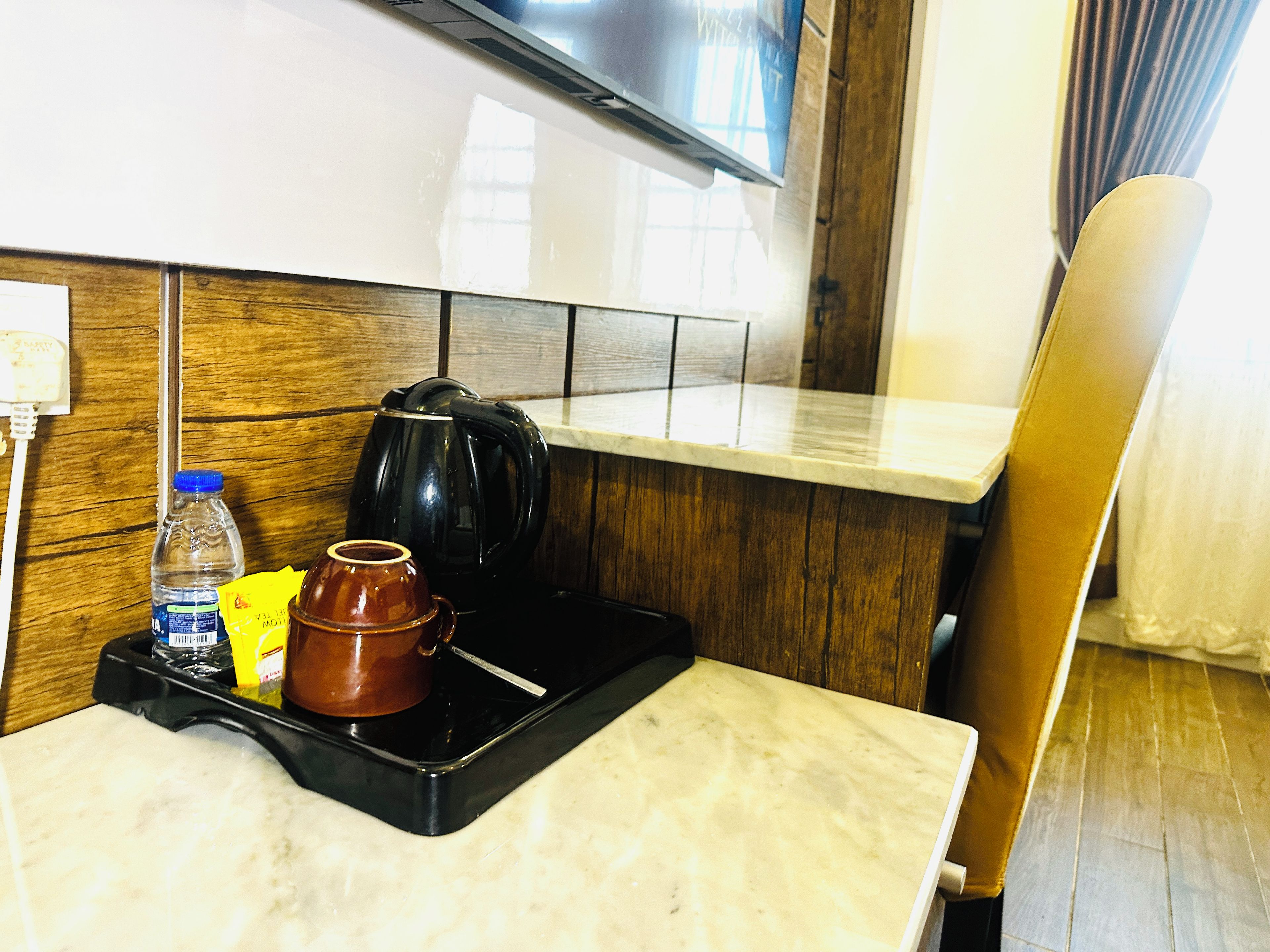 A hotel room with a kitchen area, a microwave, a kettle, a water bottle, and a tray with a cup and a spoon.