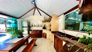 A kitchen with a brick oven, wooden cabinets, and a granite countertop. - Villa Amarela (Búzios)