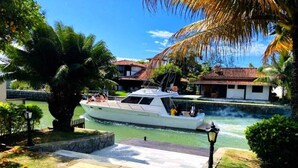 A boat docked near a canal with a pathway leading to a building with a red-tiled roof. - Villa Amarela (Búzios)