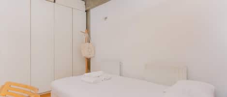 Un dormitorio con una cama, una silla de madera, un radiador y un armario.