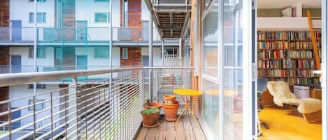 A balcony with a wooden floor, potted plants, a small table, and a chair.