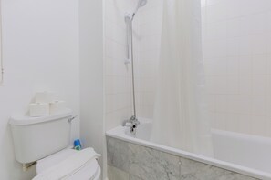 Et badeværelse med toilet, bruser og badekar.