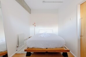 En enkeltseng med træramme i et lille rum med hvide vægge, en radiator og en trädør.