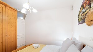 Habitación de hotel con cama, ropa de cama blanca, armario de madera y un cuadro en la pared.