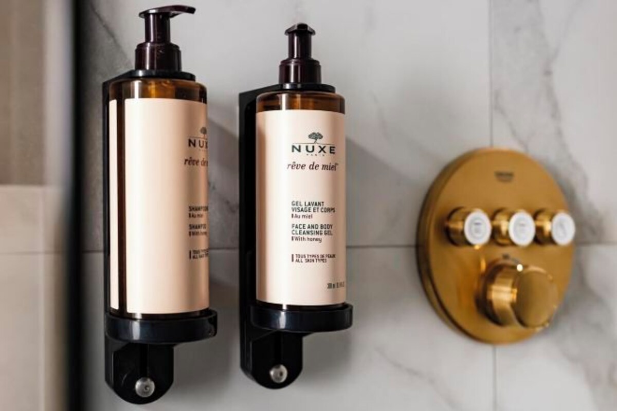 Deux flacons de produits de soins Nuxe fixés sur un mur, avec un panneau de commande de couleur dorée.