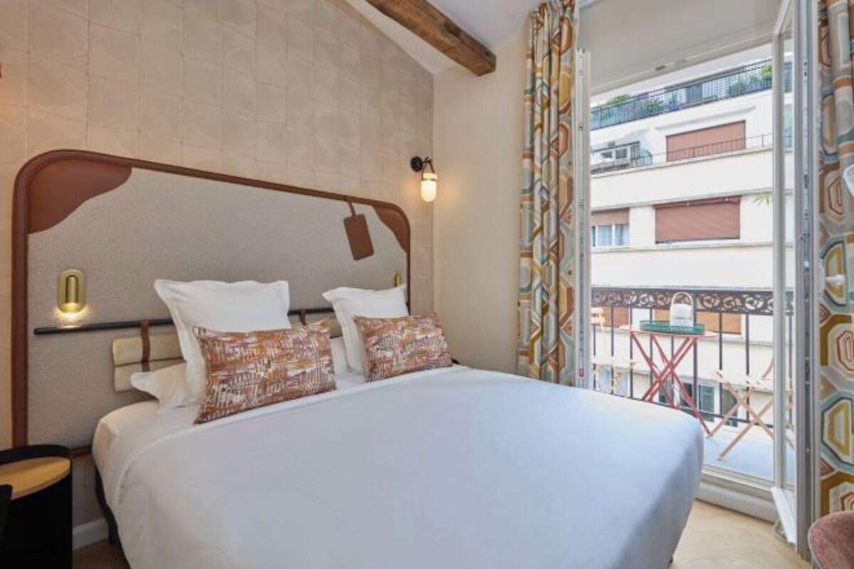 Ein Schlafzimmer mit einem großen Bett, einem Holzkopfende, einem Nachttisch und Blick auf einen Balkon mit Sitzmöbeln.