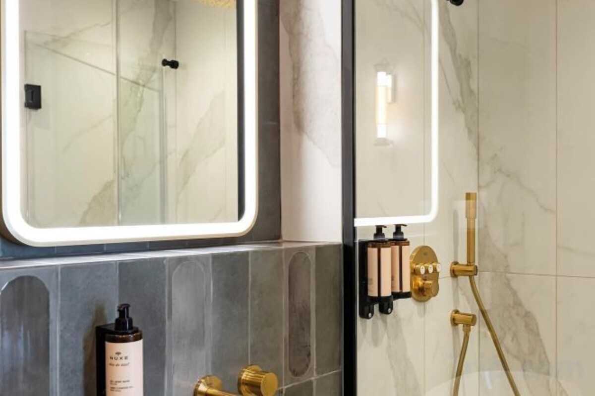 A bathroom with a glass shower enclosure, marble walls, and gold fixtures.