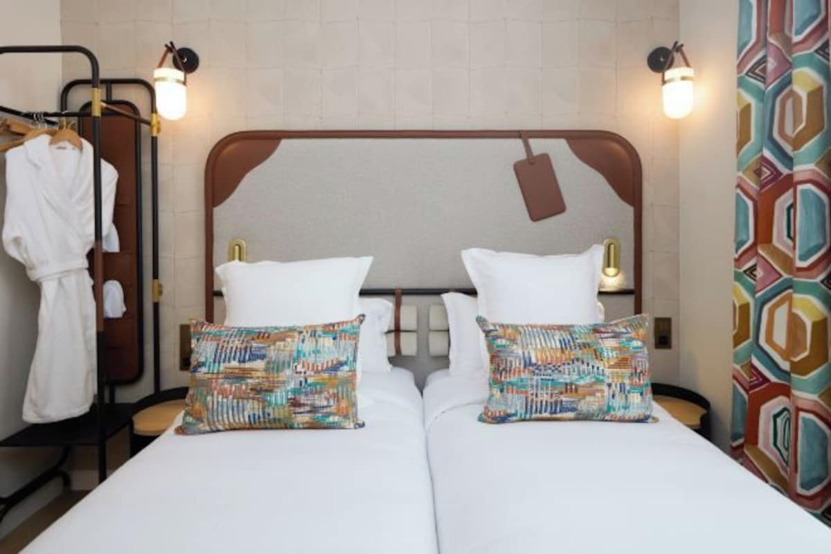 A hotel room with a double bed, two pillows, a robe rack, and a patterned curtain.