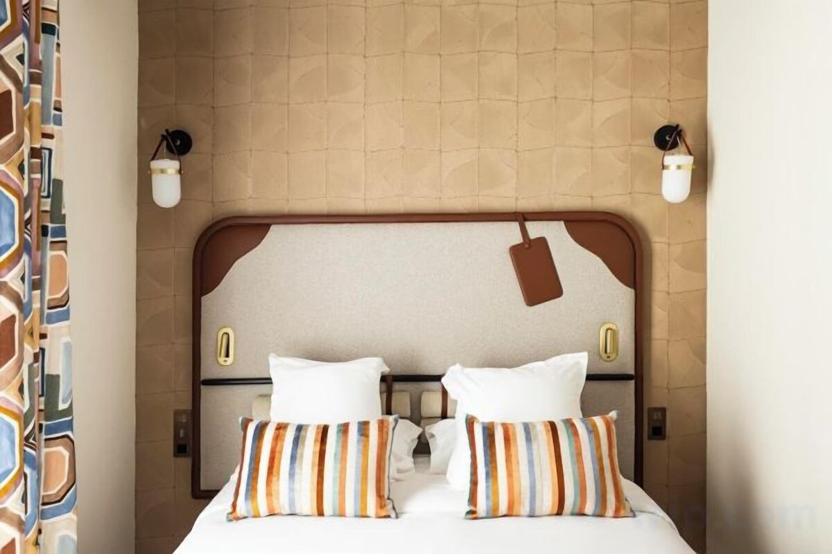 Une chambre d’hôtel avec un lit, deux tables de chevet et une tête de lit dotée d’un luminaire.