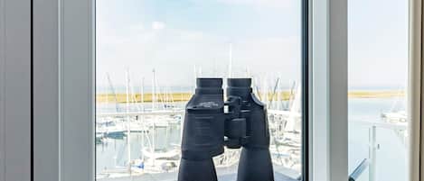 Binoculars on a table with a view of a marina through a window.