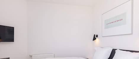 A modern bedroom with a large bed, a wall-mounted TV, and a framed quote on the wall.