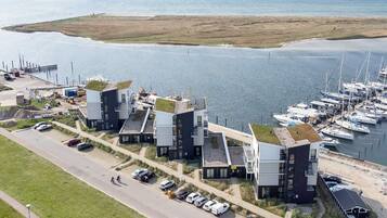 Un hotel costero de arquitectura moderna, una marina con barcos y una carretera con coches aparcados.