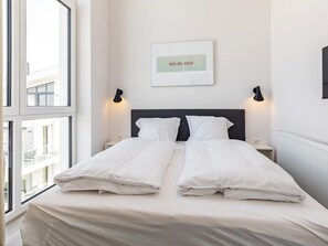 A hotel room with a bed, two bedside tables, a wall-mounted light, and a window. - 5 Star Holiday Home in Wendtorf (Wendtorf)