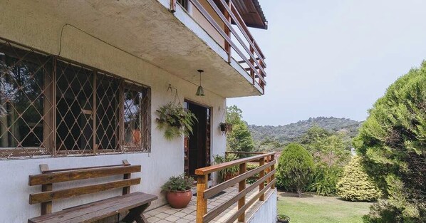 Una casa de dos pisos con balcón, banco de madera y plantas en macetas.