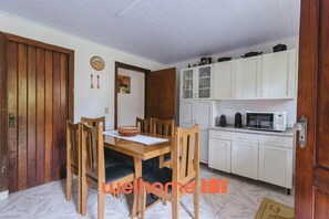 Un comedor con una mesa y sillas de madera, un armario blanco con electrodomésticos de cocina y una puerta de madera.