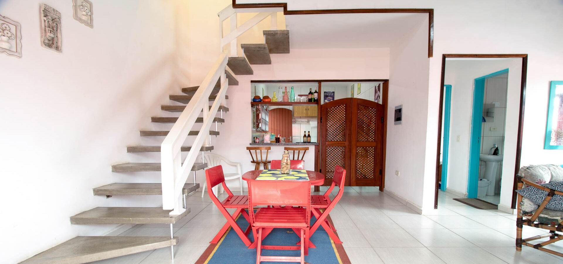 Un coin repas avec une table et des chaises rouges, un escalier et une cuisine en arrière-plan.