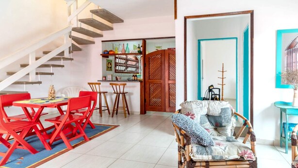 A dining area with a red table and chairs, a staircase, a kitchen area, and a living room with a patterned sofa.
