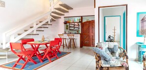Ein Essbereich mit rotem Tisch und Stühlen, eine Treppe, ein Küchenbereich und ein Wohnzimmer mit gemustertem Sofa.