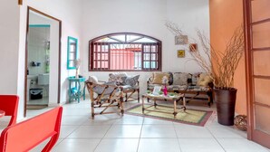 A living room with a sofa set, a coffee table, and a red chair. There is a window with bars, a door, and a potted plant.