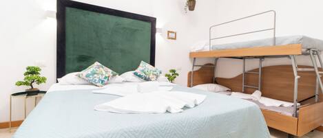 A bedroom with a large bed, a bunk bed, a green headboard, and a small potted plant.