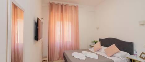 A hotel room with a bed, a bedside table, a TV, and a window with curtains.