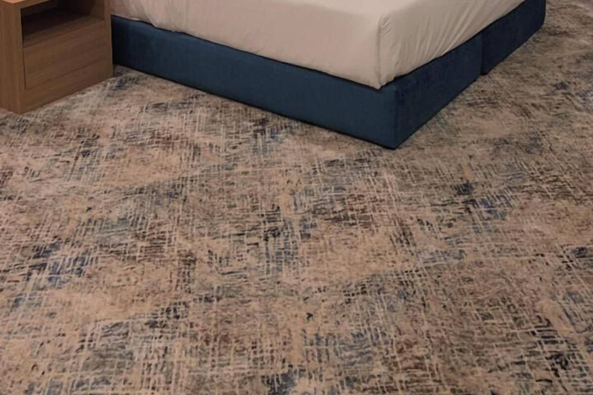 A hotel room with a large bed, two bedside tables, a nightstand, a wall-mounted lamp, and a window with curtains.