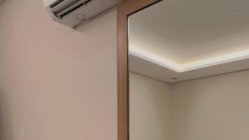 A hotel room with a wooden desk, a book, a bed with white bedding, and a ceiling-mounted air conditioner.