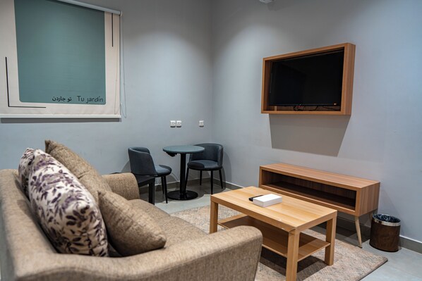 A living room with a sofa, a coffee table, a TV, and two chairs. - Holiday Plus Tabba Apartments (Madinah)