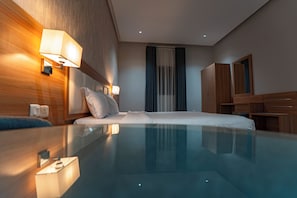 A modern hotel room with a glass-enclosed pool, wooden headboard, and a large mirror. - Holiday Plus Tabba Apartments (Madinah)