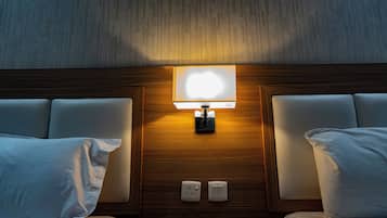 A hotel room with a wooden headboard, two white pillows, a bedside table, and a wall-mounted lamp.