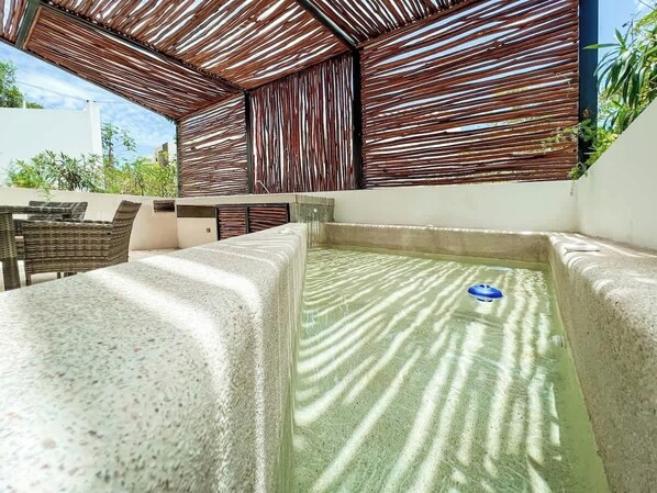 An outdoor hot tub area with a stone bench, a wicker chair, and a bamboo ceiling.