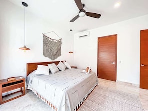 A bedroom with a bed, bedside tables, a ceiling fan, an air conditioning unit, and a wooden door.